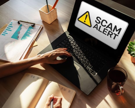 Hands typing on a laptop displaying a "scam alert" warning on its screen