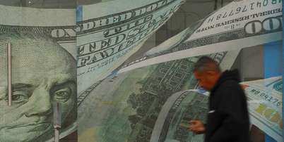 Um homem passa em frente a uma casa de c&acirc;mbio, com adesivos de notas de d&oacute;lar na porta e nas paredes Foto: Reuters