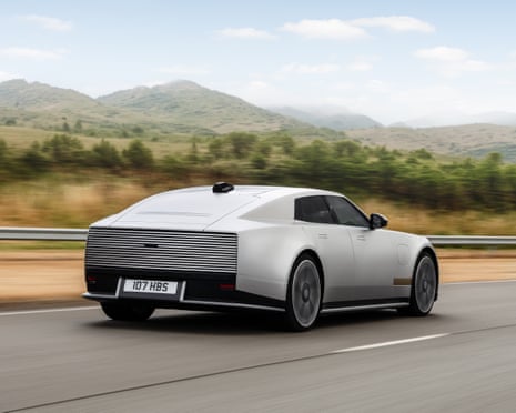A sleek silver Jaguar concept car drives along a road with hills in the background