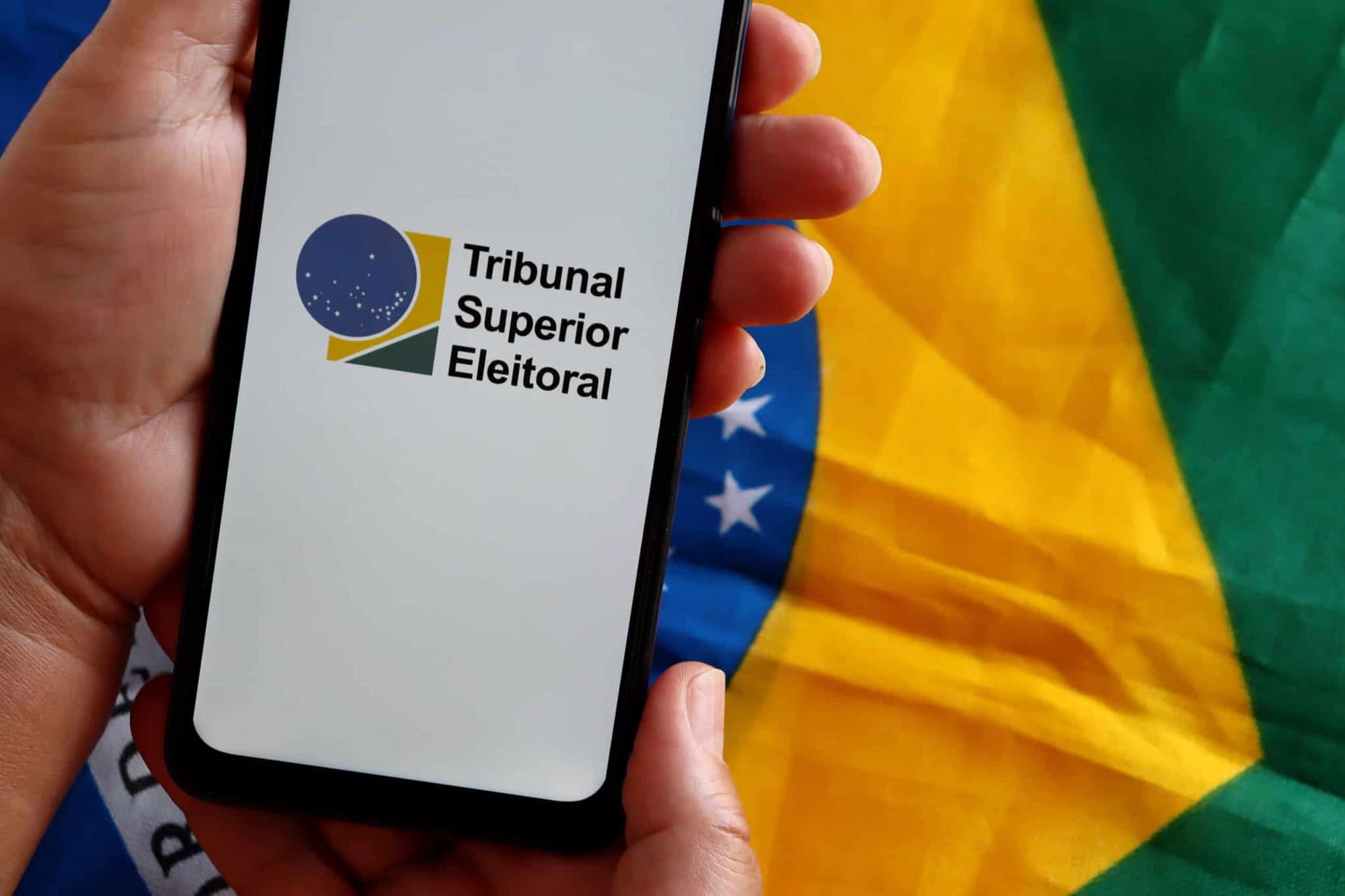 Pessoa segurando um smartphone com o logo do Tribunal Superior Eleitoral