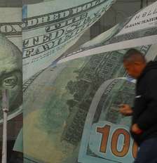 Um homem passa em frente a uma casa de câmbio, com adesivos de notas de dólar na porta e nas paredes Foto: Reuters