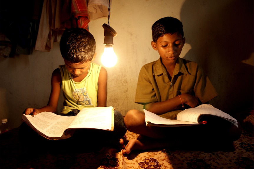 Two boys with school books are sitting under a naked light bulb at night