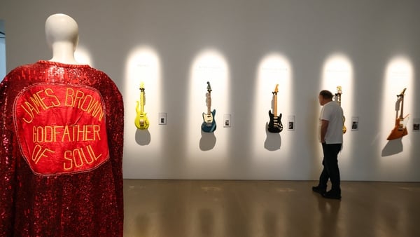 (L-R) James Brown's stage-worn sequined cape is displayed as a visitors looks at (L-R) Prince's Andy Beech custom Yellow Cloud guitar, Kurt Cobain's 1966 Fender Mustang, David Gilmour's "Black Strat", Eric Clapton’s "The Fool" Gibson SG and The Edge's Gib